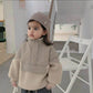 Child wearing a beige coat and knit hat indoors