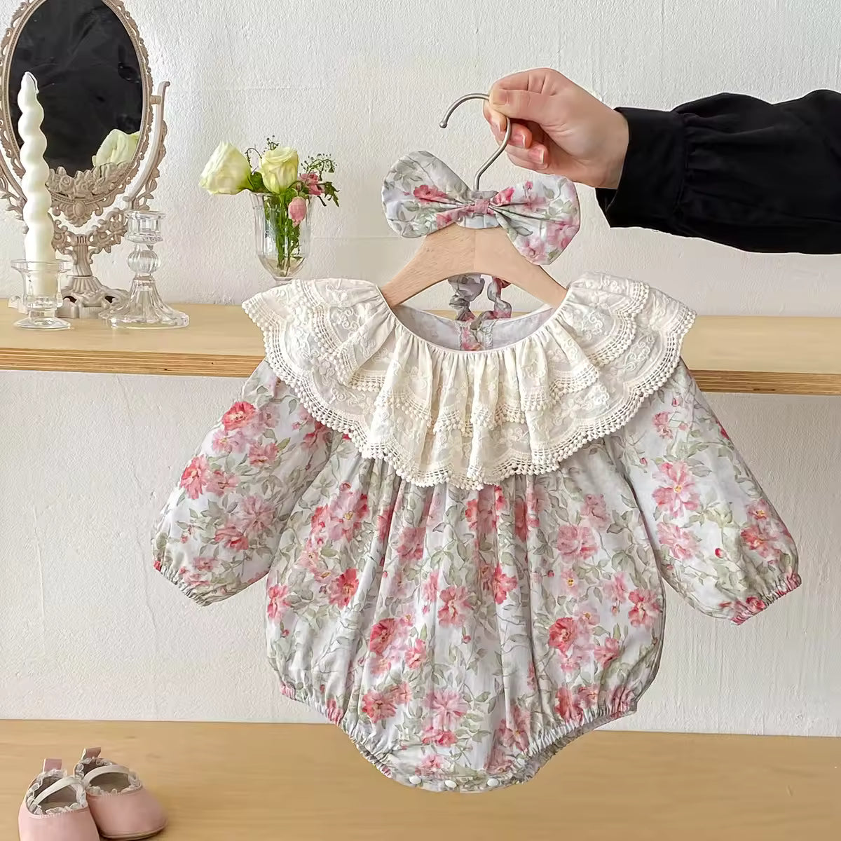 Floral baby romper with lace collar on a hanger against a neutral background